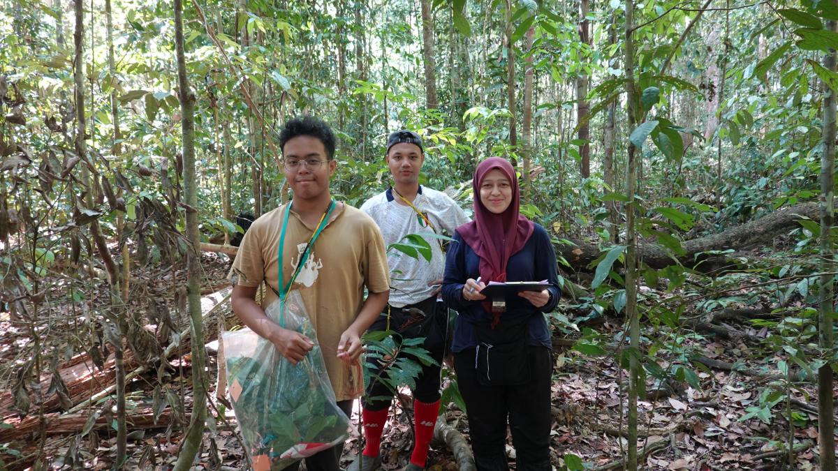 3 individuals smile at the camera while holding clipboards in a forest