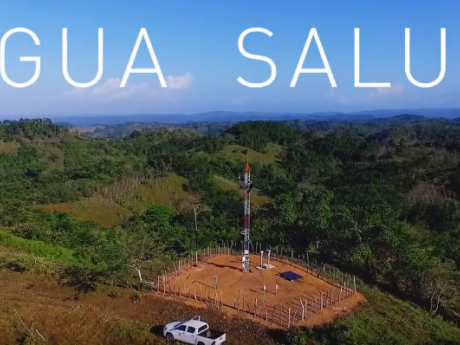 White text reading, “Agua Salud” over a landscape photo of blue sky, patchy green forest, and a red and white observation tower.